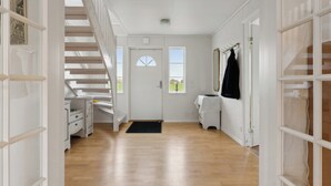 Ein Flur mit Holzboden, einer weißen Tür, einer Treppe und einem Kleiderständer.