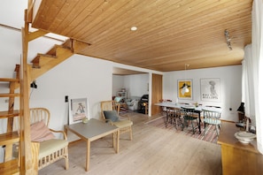 A spacious living area with a wooden staircase, a dining table with chairs, and a kitchen area in the background. - Cozy cottage on North Bornholm (Hasle)