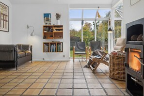 Ein Wohnzimmer mit Kamin, einer Couch, einem Sessel, einem Bücherregal und einem großen Fenster.