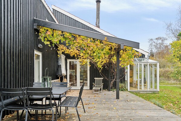 Ein modernes Gebäude mit überdachter Terrasse, einem Glashaus und einer Holzterrasse.