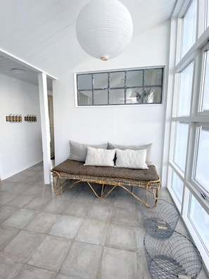 Una habitación con un sofá de ratán, un ventanal grande y una lámpara colgante.