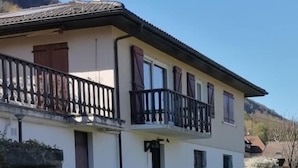 Un edificio de dos pisos con balcón, chimenea y ventana con cortinas.