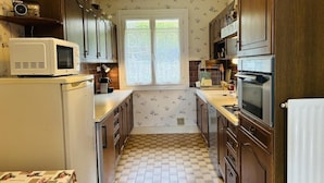 Cocina compacta con armarios de madera, microondas y ventana con vistas a zonas verdes.
