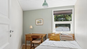 Een slaapkamer met een bed, een bureau, een stoel, een raam met jaloezieën en een plafondlamp.