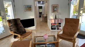 Een woonkamer met een televisie, twee stoelen, een bijzettafeltje met boeken en een boekenkast.