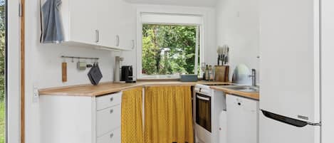 Una cocina compacta con armarios blancos, una ventana y vista a zonas verdes.