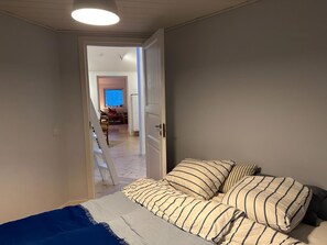 A bedroom with a bed, pillows, and a door leading to another room.