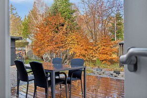 Una terraza de madera con una mesa y sillas, rodeada de follaje otoñal.