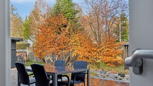 Eine Holzterrasse mit Tisch und Stühlen, umgeben von herbstlichem Laub.