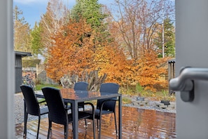 A wooden deck with a table and chairs, surrounded by autumn foliage. - Cozy summer house near beach and nature (Væggerløse)