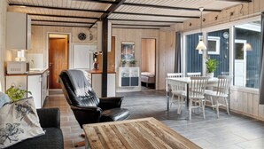 Ein modernes Interieur mit Holzbalkendecke, einem Essbereich mit weißen Stühlen, einer schwarzen Ledersofa und einer Küchenzeile.