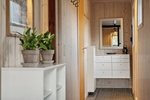 A narrow hallway with wooden walls, a white dresser, a mirror, and potted plants. - Cozy summer house near beach and nature (Væggerløse)
