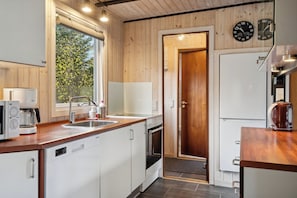 A modern kitchen with wooden walls, a sink, a stove, and a refrigerator. - Cozy summer house near beach and nature (Væggerløse)