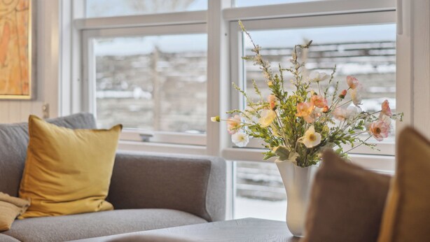 A living room with a sofa, a vase of flowers, and a window with a view. - Cozy beach bungalow close to Balka Beach (Nexø)