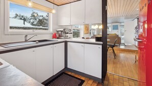A modern kitchen with a window, wooden ceiling, and a view of a snowy landscape. - Cozy beach bungalow close to Balka Beach (Nexø)