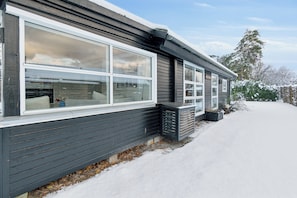 Una casa moderna con ventanas grandes, fachada oscura y entrada cubierta de nieve.