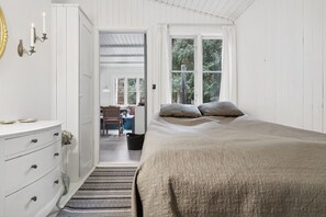 A bedroom with a bed, a dresser, a window, and a door leading to another room.
