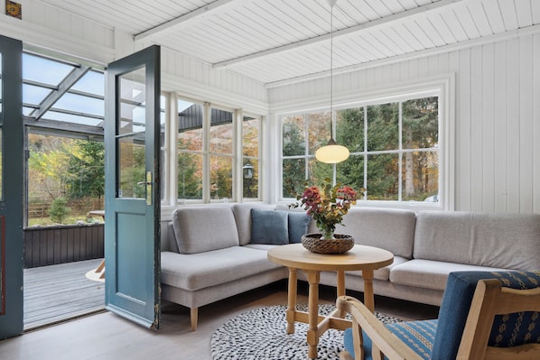 A room with a large window, a sofa, a round wooden table, and a door.
