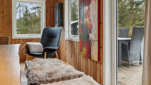 A room with wooden walls, a large window, a chair, a table, and a rug.