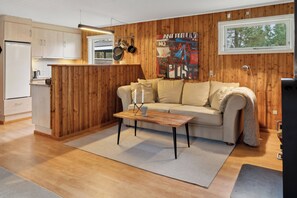A modern kitchen with wooden paneling, a dining area with a sofa and table, and a large window with a view of trees.
