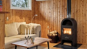 A cozy room with a wooden interior, a sofa, a table with candles, and a wood-burning stove.