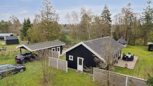 A black building with a white door, surrounded by a fenced yard with a picnic table and chairs.