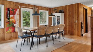 A dining area with a wooden table and chairs, a large window, and a view of trees.