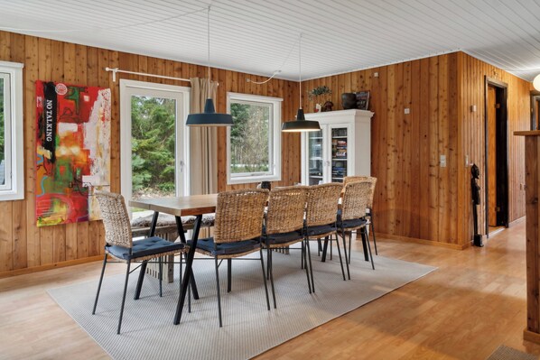 A dining area with a wooden table and chairs, a large window, and a view of trees.