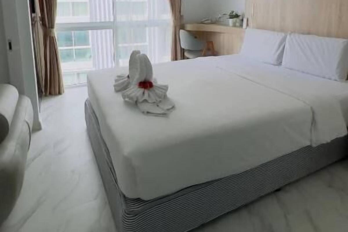 A modern hotel room with a neatly made bed, a desk, and a large window with curtains.