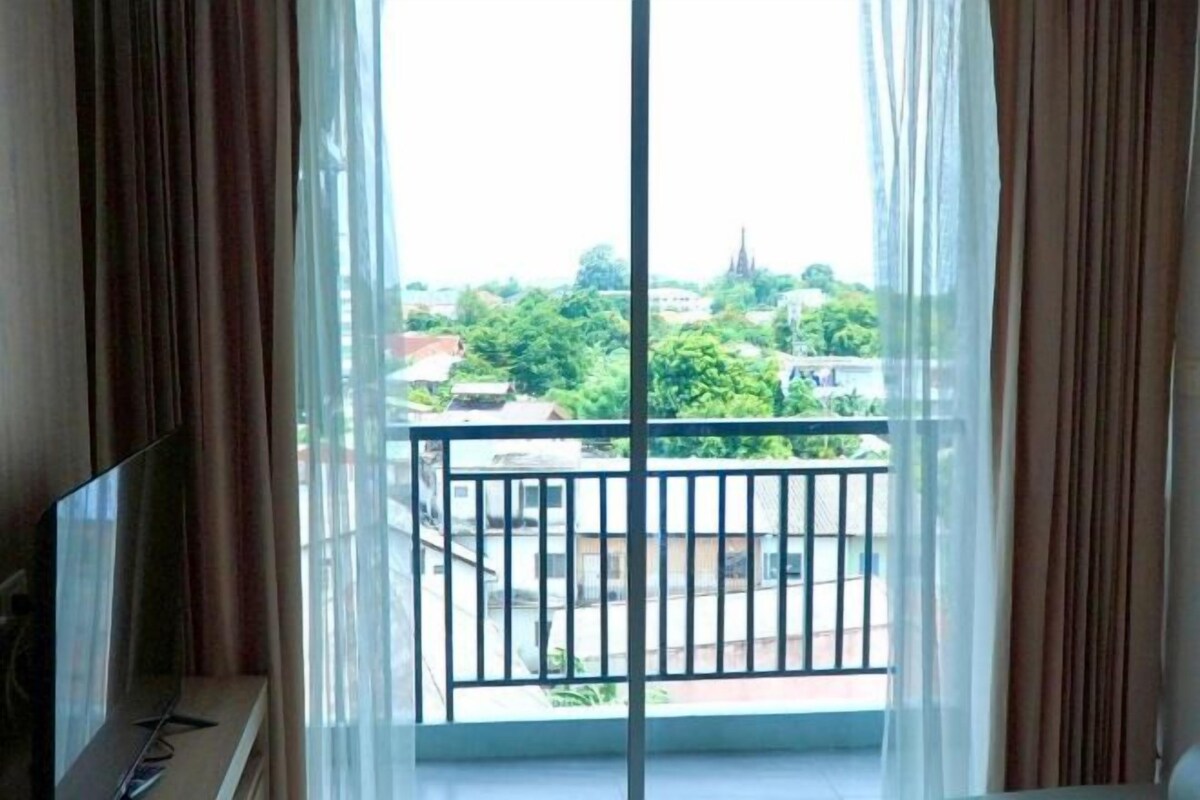 A room with a large window, a TV on a stand, and a balcony with a railing.