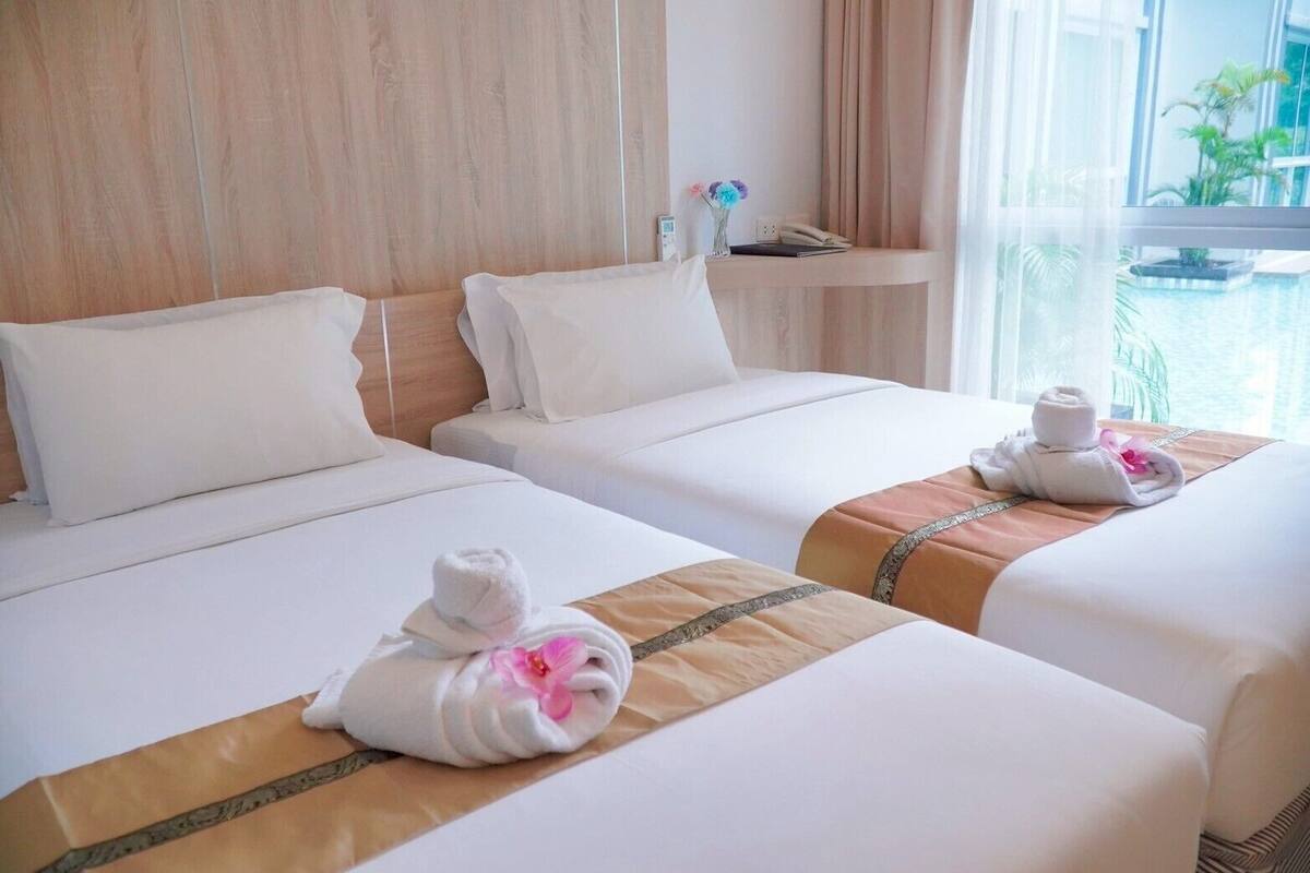 A hotel room with two beds, each with white linens and a brown decorative strip. There are towels with pink flowers on the beds.