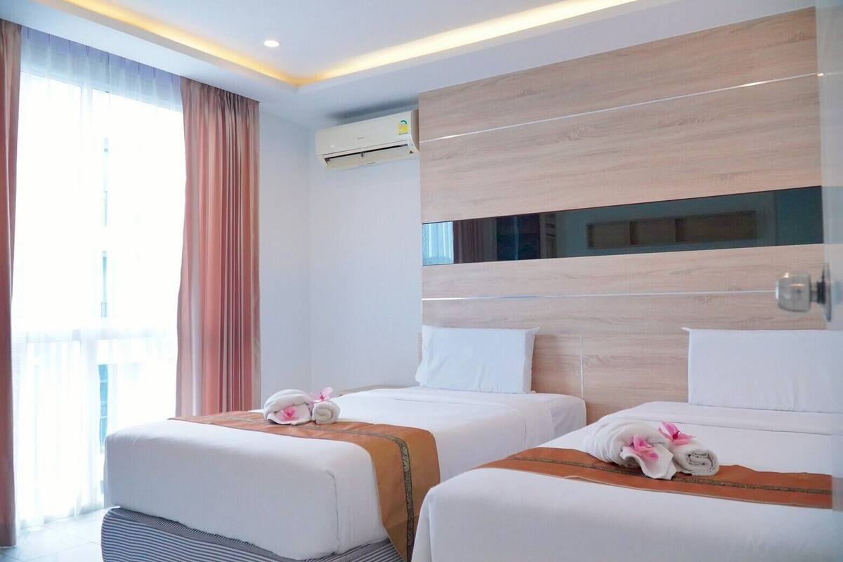 A hotel room with two beds, a large window with curtains, an air conditioning unit, and a wooden headboard.