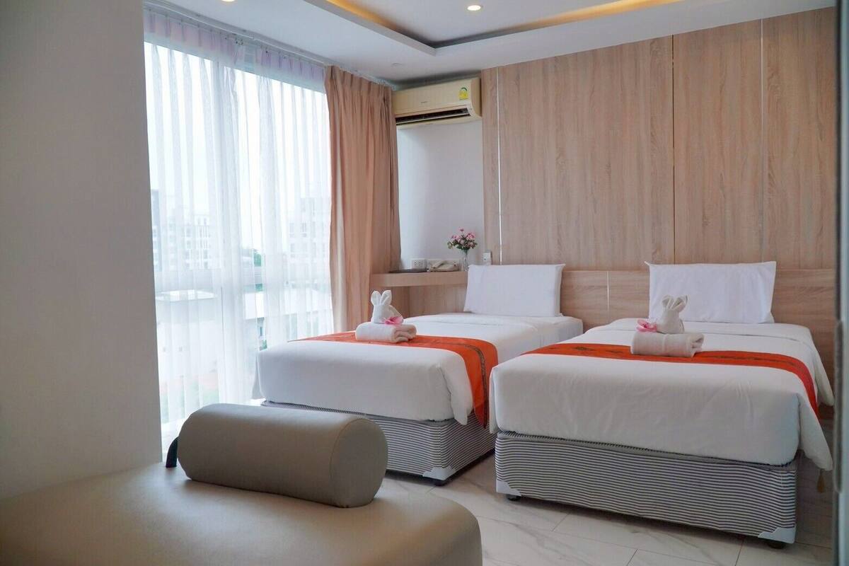 A hotel room with two beds, a sofa, and a large window with curtains.