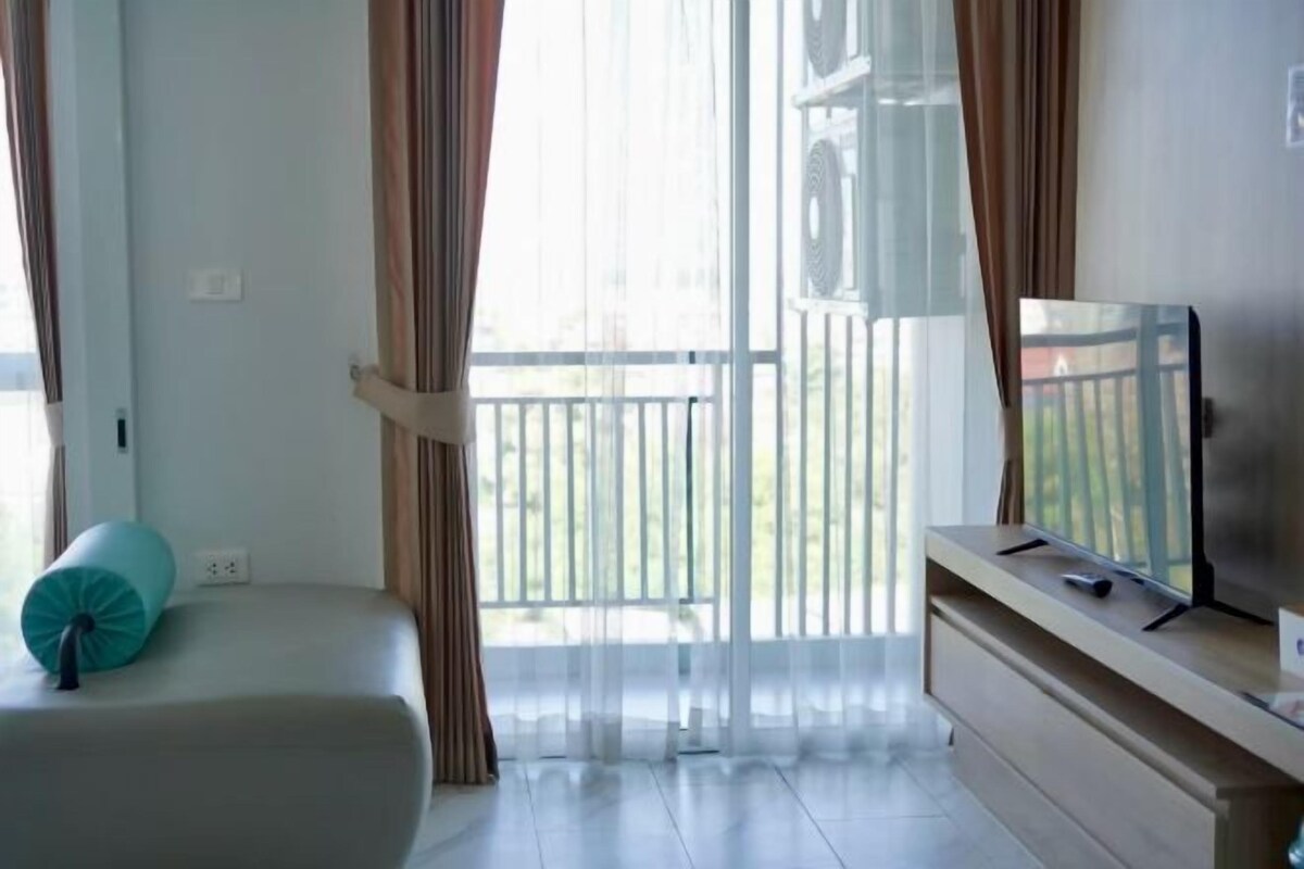 A hotel room with a bed, a TV on a wooden stand, and a balcony with curtains.