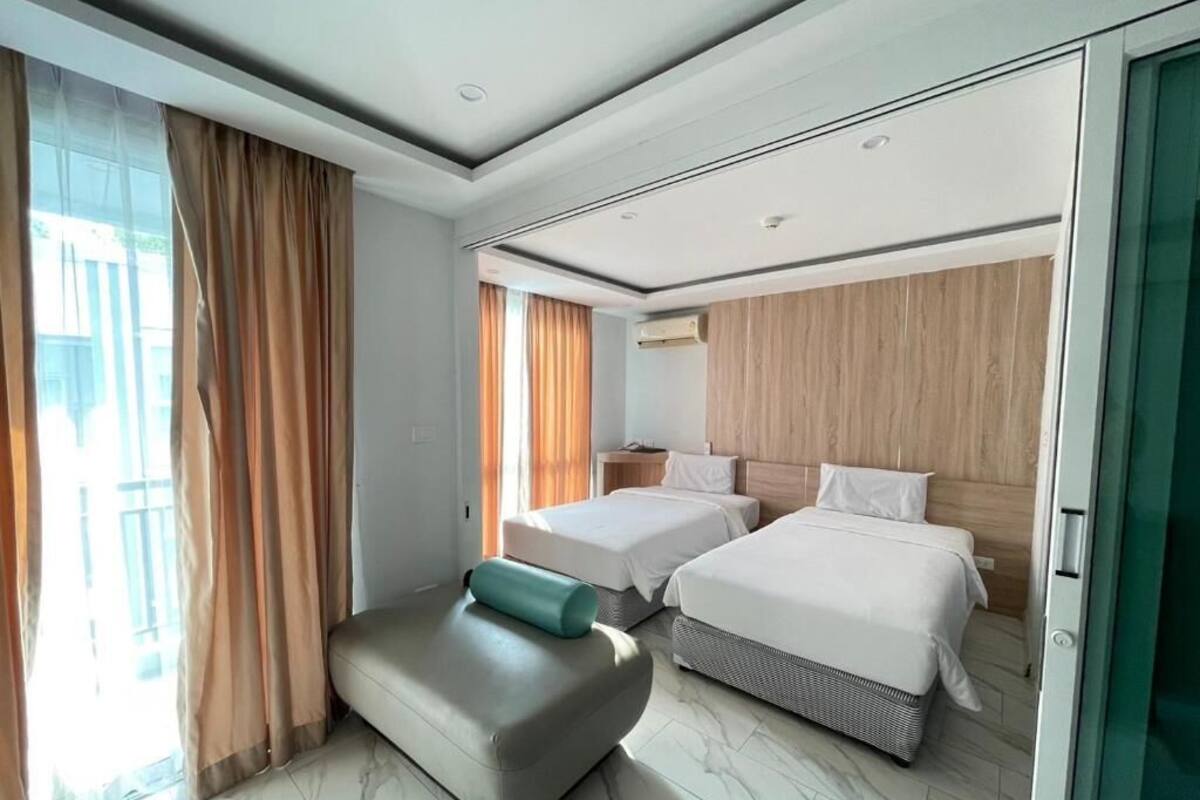 A modern hotel room with two beds, a sofa, and a large window with curtains.