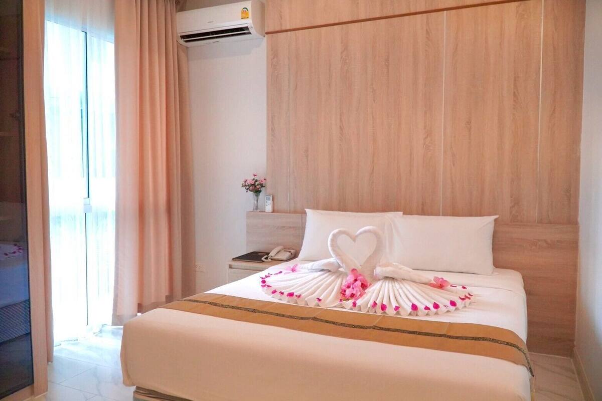 A hotel room with a neatly made bed, a bedside table with a phone, and a wall-mounted air conditioner.