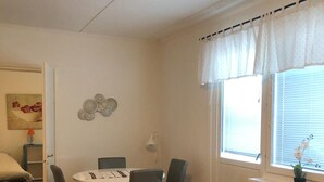 A living room with a sofa, armchair, dining table, chairs, and a window with curtains. - Holiday Home Bispgården (Bispgården)