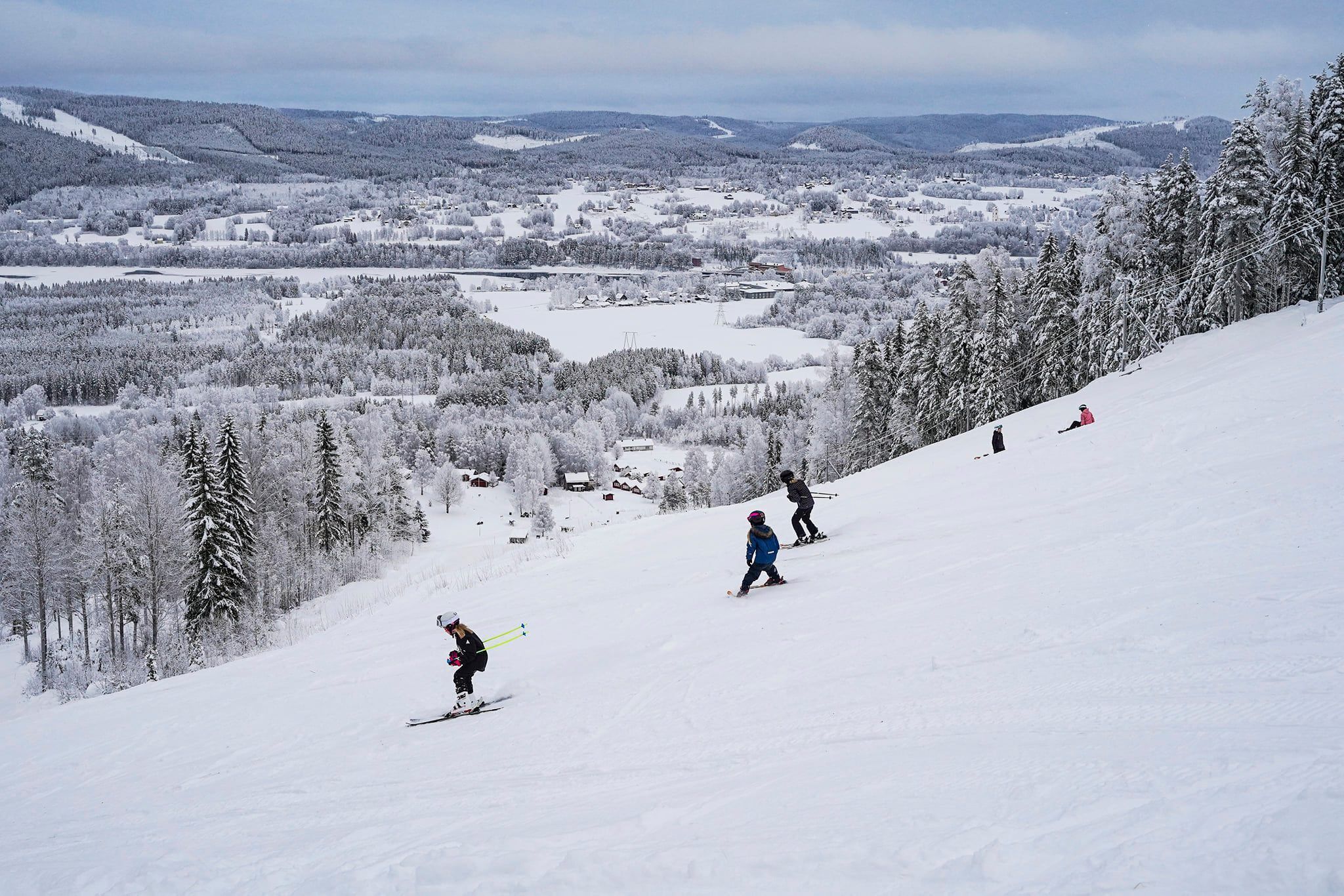 A snowy ski slope with skiers and a panoramic view of a winter landscape.