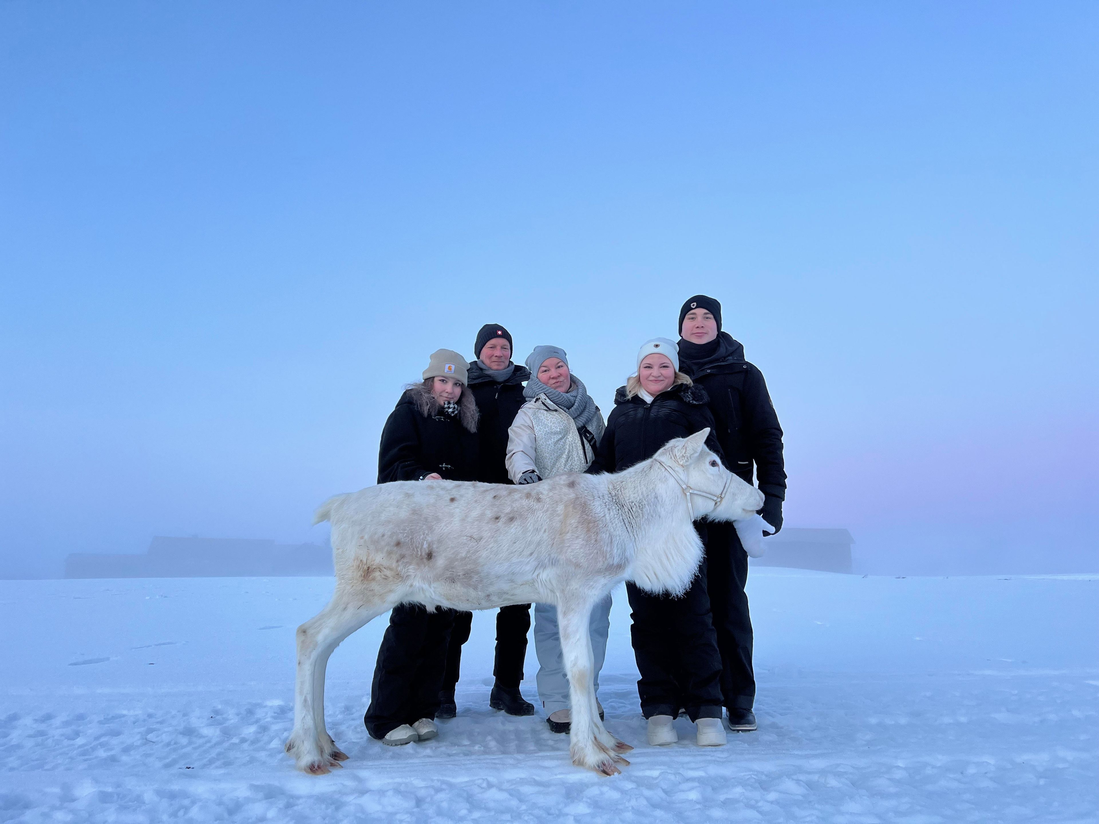 Un groupe de personnes se tient sur une surface enneigée, avec un grand chien blanc au premier plan.
