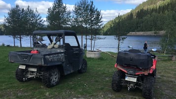 Deux véhicules tout-terrain sont stationnés sur une zone herbeuse près d’un lac, avec des arbres et des collines en arrière-plan.