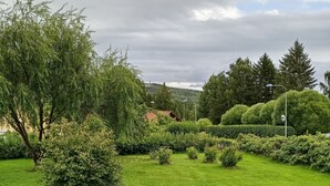 A well-maintained garden with various shrubs and a lawn, a white fence, and a distant view of a red-roofed building. - Holiday Home Bispgården (Bispgården)