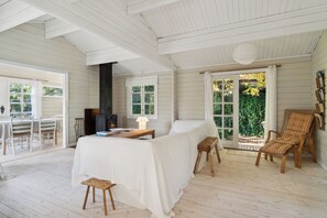 A room with a fireplace, a dining table with chairs, a sofa, a chair, and a large window with curtains.