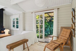 A cozy room with a wooden bench, a striped chair, a fireplace, and a large window with curtains.