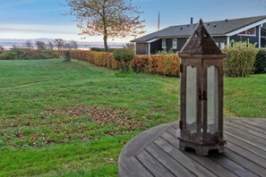 Un espace extérieur verdoyant avec une terrasse en bois, une lanterne et une maison en arrière-plan.