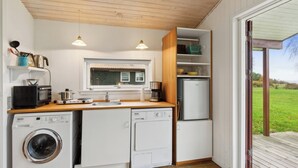 A compact kitchen with a washing machine, microwave, and a refrigerator. - Cozy little annex with a sea view. (Kalvehave)