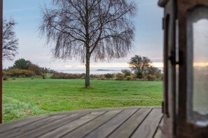 A view from a window overlooking a grassy field with a tree and distant horizon.