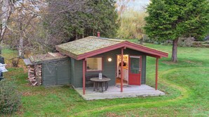 A small wooden cabin with a porch, a table, and a chair. - Cozy little annex with a sea view. (Kalvehave)