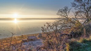 A serene lakeside view with a clear sky, calm water, and sparse vegetation. - Cozy little annex with a sea view. (Kalvehave)