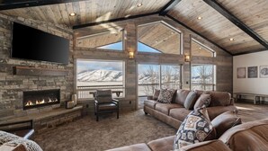 Un amplio salón con chimenea de piedra, sofás de cuero y grandes ventanales con vistas a la montaña.