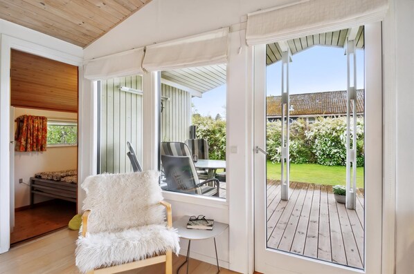 A room with a white furry chair, a small table, and a view of a wooden deck and garden.